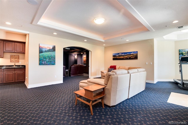 living room featuring a textured ceiling, sink, dark carpet, and a raised ceiling