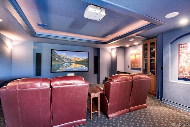 carpeted home theater room with a tray ceiling and a textured ceiling