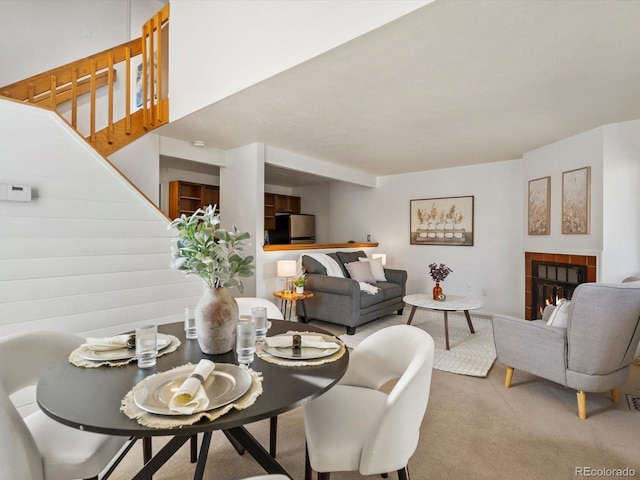 carpeted dining space featuring a tiled fireplace and stairs