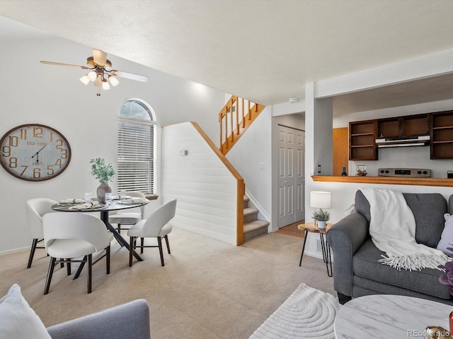 living area with baseboards, stairway, a ceiling fan, and light carpet