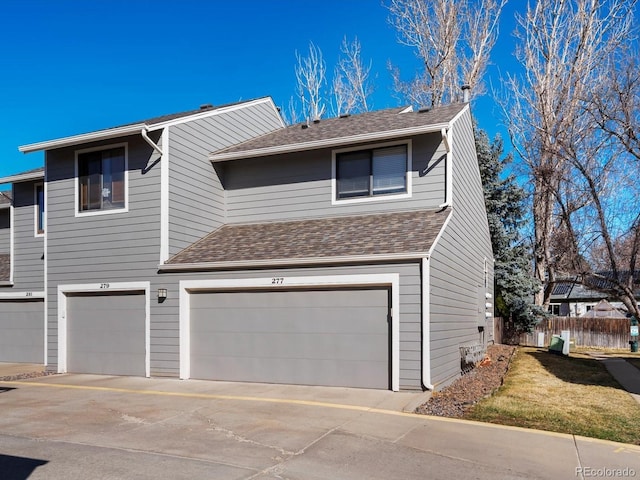 view of front facade with fence, a shingled roof, an attached garage, and concrete driveway