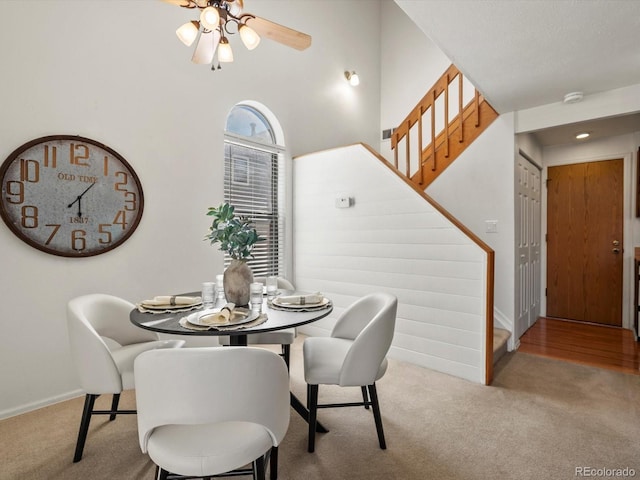 carpeted dining room with baseboards, ceiling fan, and stairway