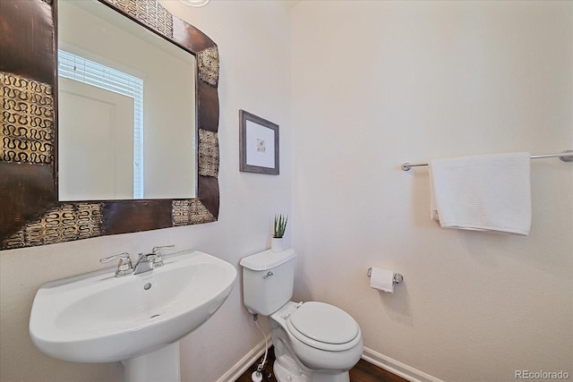 half bathroom with a sink, toilet, and baseboards