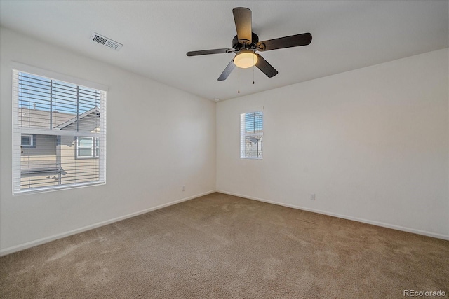 carpeted spare room featuring baseboards, visible vents, and ceiling fan