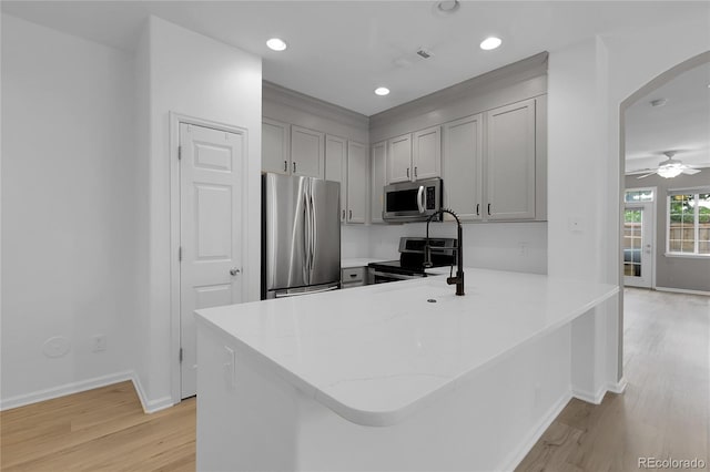 1409 Carlyle Park Cir, Highlands Ranch, CO 80129 - kitchen with appliances with stainless steel finishes, arched walkways, light wood finished floors, a peninsula, and gray cabinetry