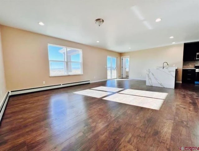 unfurnished living room with baseboards, dark wood-style flooring, a baseboard heating unit, a sink, and recessed lighting