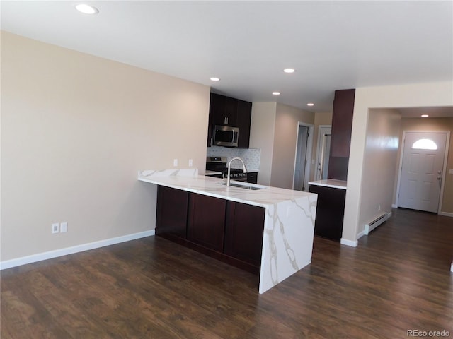 kitchen featuring a baseboard radiator, a peninsula, a sink, stainless steel microwave, and dark wood finished floors