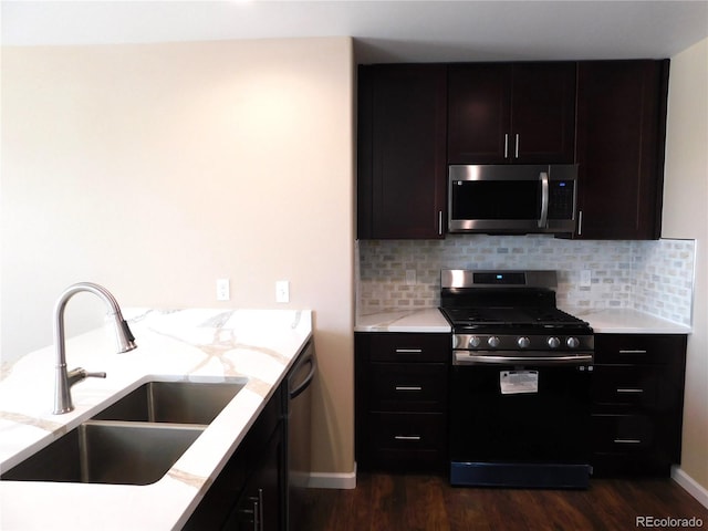 kitchen featuring tasteful backsplash, dark wood finished floors, stainless steel microwave, gas range oven, and a sink