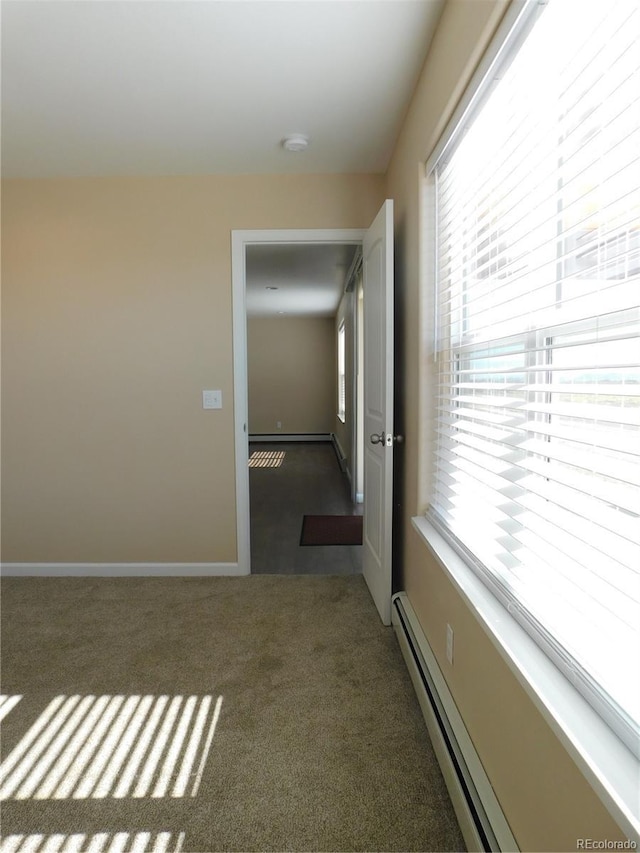 spare room featuring a baseboard heating unit, carpet, and baseboards