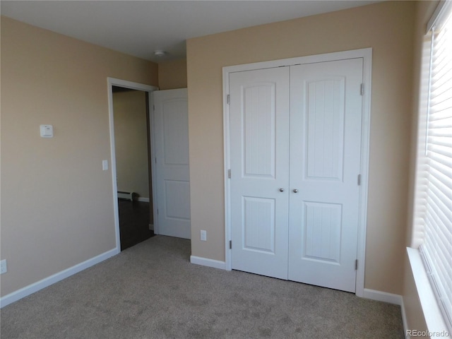 unfurnished bedroom featuring carpet floors, a baseboard radiator, baseboards, and a closet