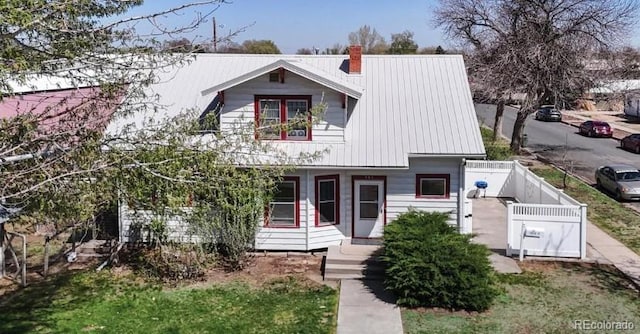 view of front of property with covered porch, metal roof, a chimney, and fence