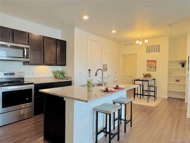 kitchen with decorative light fixtures, an island with sink, sink, stainless steel appliances, and washer and clothes dryer