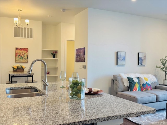 kitchen featuring pendant lighting, light stone countertops, sink, and a notable chandelier