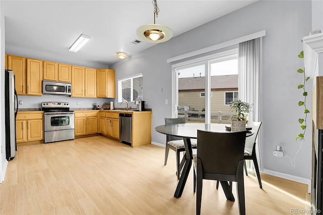 kitchen featuring light wood finished floors, stainless steel appliances, light brown cabinets, and a sink