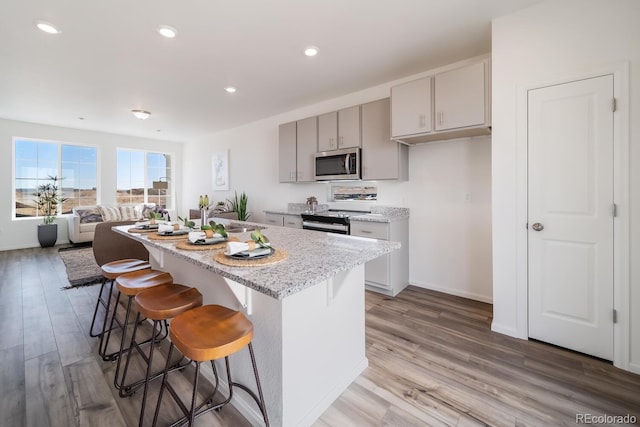 kitchen featuring gray cabinetry, a breakfast bar, appliances with stainless steel finishes, light wood-style floors, and a kitchen island with sink