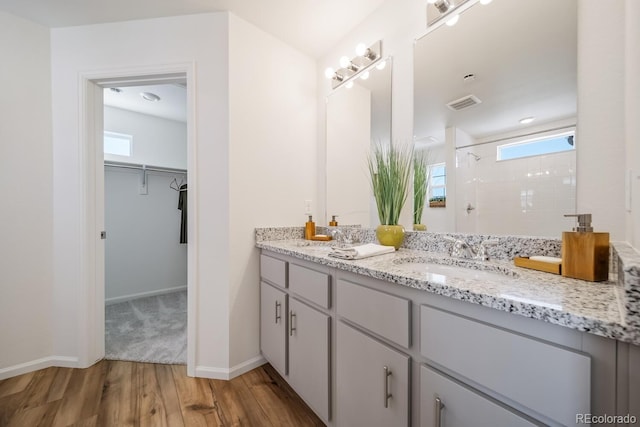 bathroom with visible vents, a walk in closet, a sink, wood finished floors, and a tile shower