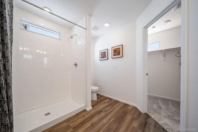 bathroom featuring wood finished floors, visible vents, a tile shower, a walk in closet, and toilet