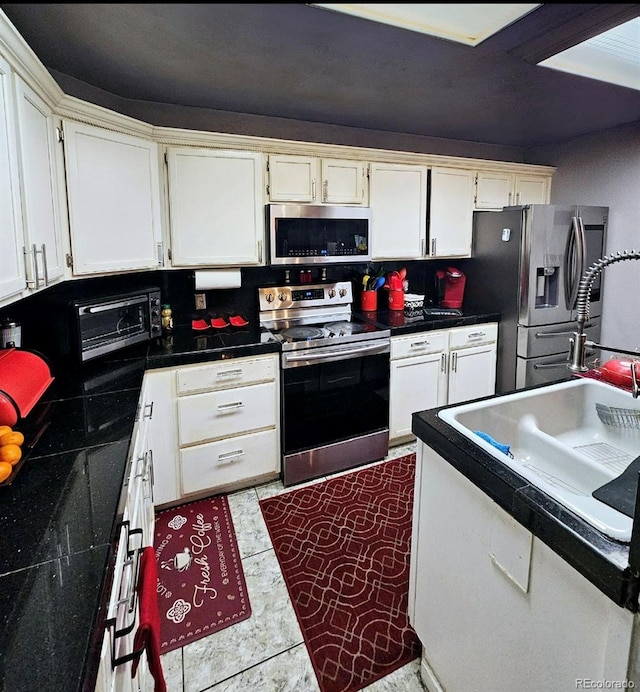 kitchen with a sink, white cabinets, appliances with stainless steel finishes, and dark countertops