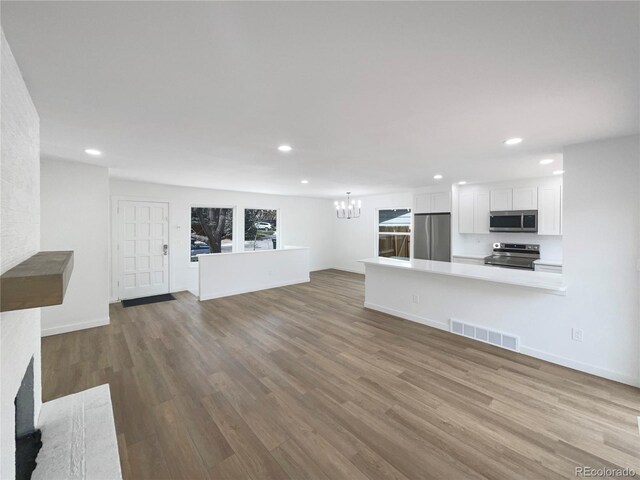 unfurnished living room with visible vents, recessed lighting, wood finished floors, and an inviting chandelier