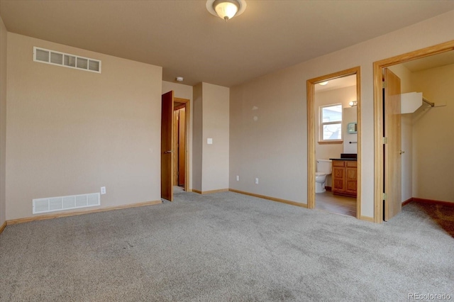 unfurnished bedroom with connected bathroom, a spacious closet, a closet, and light colored carpet