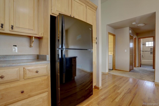 kitchen with light wood finished floors, washer / dryer, freestanding refrigerator, light countertops, and light brown cabinetry