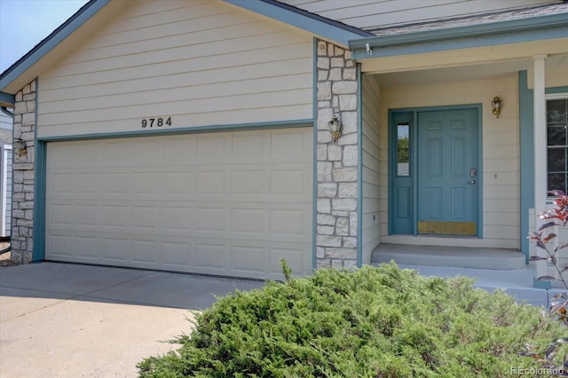 doorway to property with a garage, stone siding, and driveway