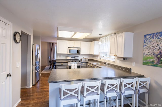 kitchen featuring pendant lighting, sink, white cabinets, kitchen peninsula, and stainless steel appliances