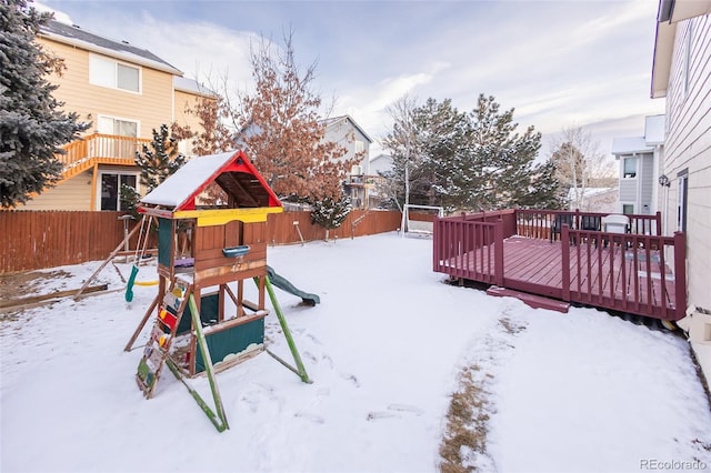 snowy yard with a playground and a deck