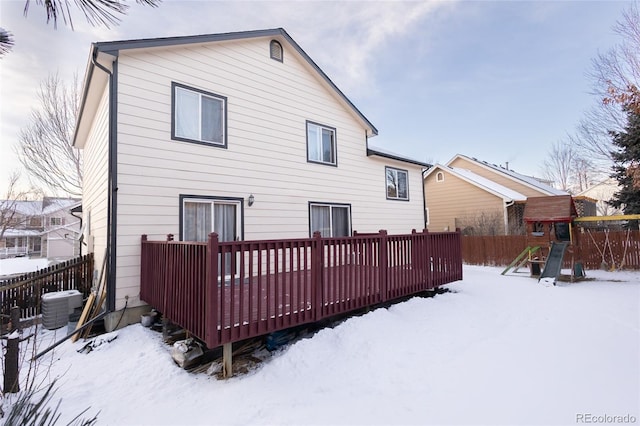 snow covered rear of property with a playground, a wooden deck, and central air condition unit