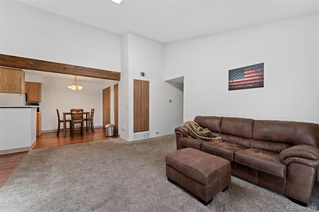 carpeted living area with visible vents, wood finished floors, a chandelier, and high vaulted ceiling