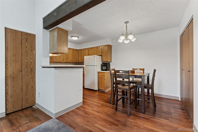 kitchen featuring a textured ceiling, brown cabinets, freestanding refrigerator, dark wood-style floors, and an inviting chandelier