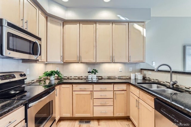 kitchen featuring light brown cabinetry, sink, dark stone countertops, decorative backsplash, and stainless steel appliances