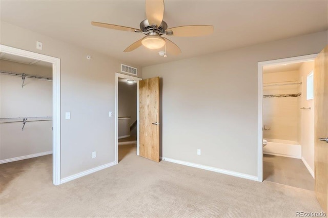 unfurnished bedroom with a walk in closet, ensuite bath, a closet, ceiling fan, and light carpet