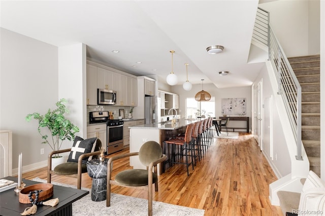 kitchen featuring white cabinets, light stone countertops, an island with sink, decorative light fixtures, and stainless steel appliances