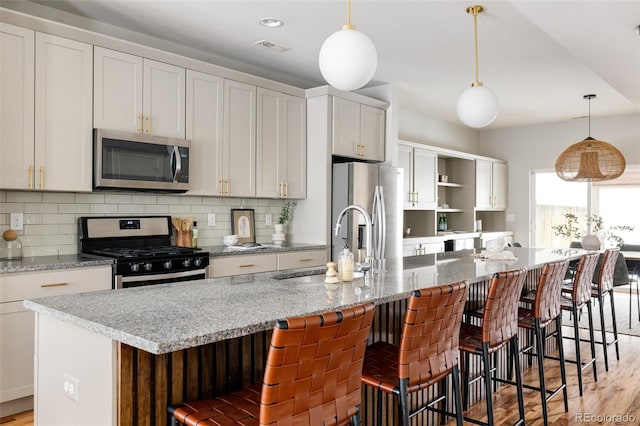 kitchen with decorative light fixtures, a kitchen bar, stainless steel appliances, and a large island with sink