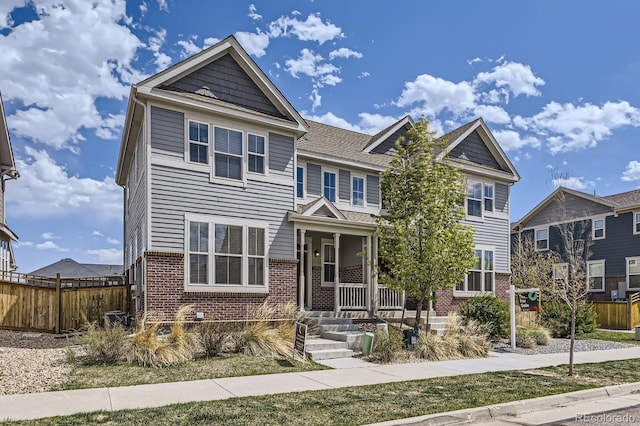 townhome / multi-family property featuring brick siding, covered porch, and fence