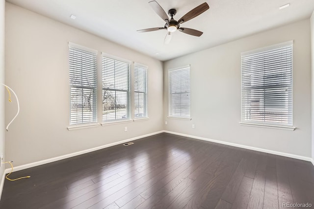 empty room featuring visible vents, a ceiling fan, baseboards, and dark wood finished floors