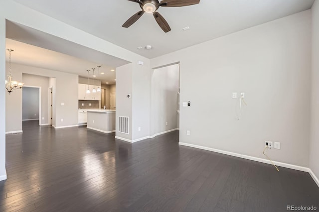 unfurnished living room with ceiling fan with notable chandelier, baseboards, visible vents, and dark wood-type flooring