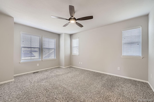 carpeted spare room with visible vents, baseboards, and ceiling fan