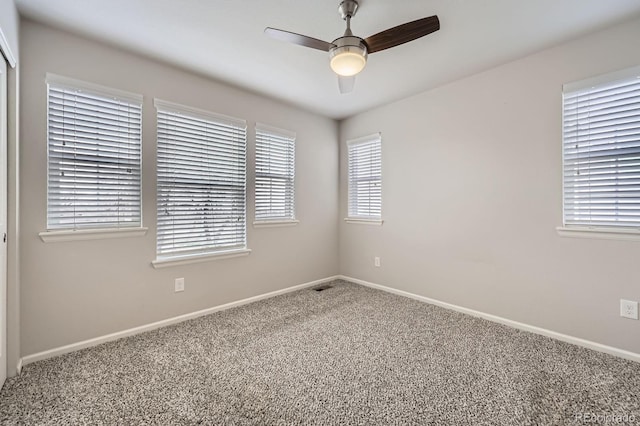 carpeted empty room featuring a healthy amount of sunlight, a ceiling fan, baseboards, and visible vents