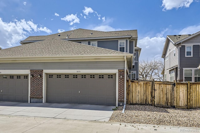 traditional-style house with roof with shingles, driveway, fence, brick siding, and an attached garage