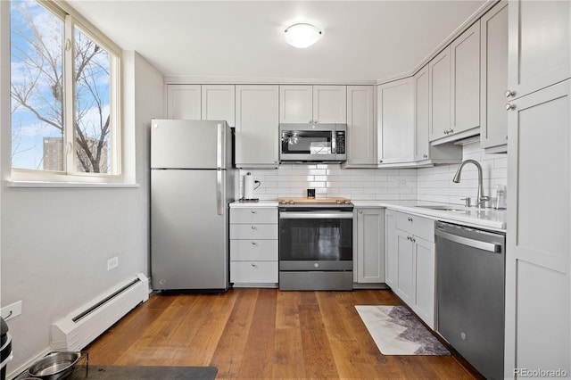 kitchen featuring wood finished floors, a sink, stainless steel appliances, a baseboard heating unit, and backsplash