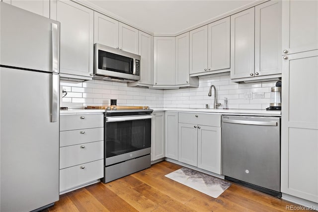 kitchen with stainless steel appliances, a sink, backsplash, and light wood finished floors