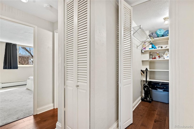 hallway featuring a baseboard heating unit, a textured ceiling, dark wood-style floors, and baseboards