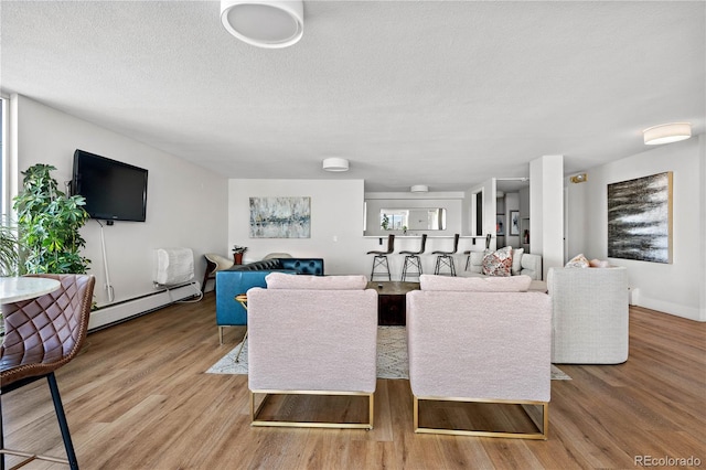 living area with light wood-type flooring, a baseboard heating unit, and a textured ceiling