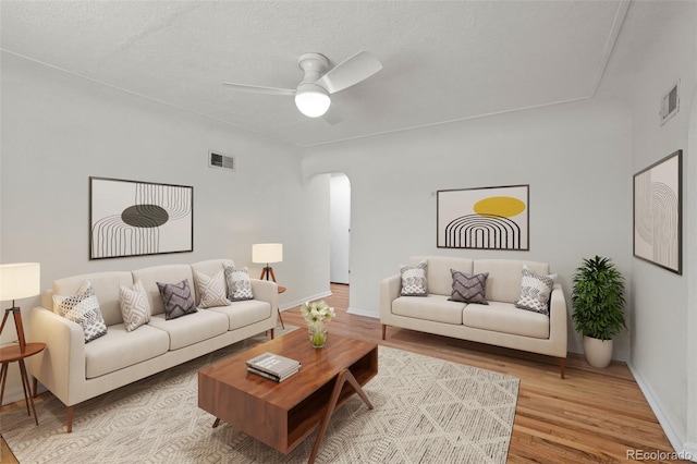 living room featuring arched walkways, light wood-type flooring, ceiling fan, baseboards, and a textured ceiling