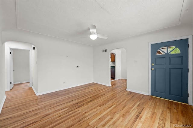 entryway with arched walkways, a ceiling fan, light wood-style flooring, a textured ceiling, and baseboards