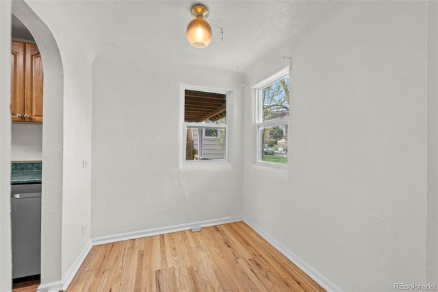 spare room with light wood-style floors, baseboards, and arched walkways