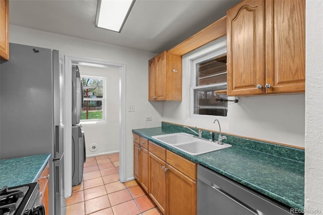kitchen featuring stainless steel appliances, a sink, light tile patterned floors, and dark countertops