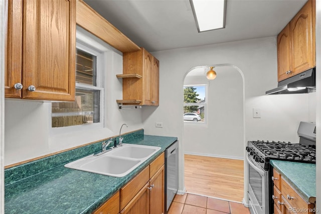 kitchen with appliances with stainless steel finishes, under cabinet range hood, a sink, arched walkways, and light tile patterned floors